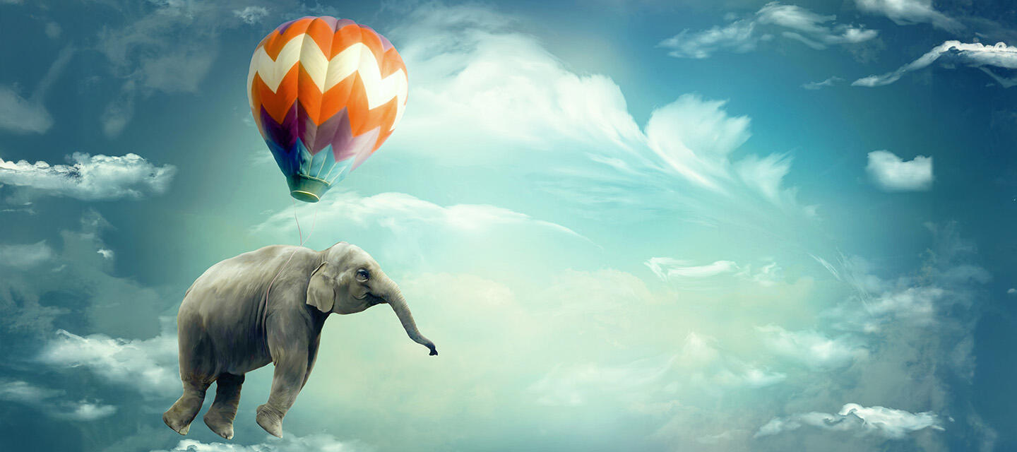 An elephant carried by a hot air ballon in a beautiful blue sky